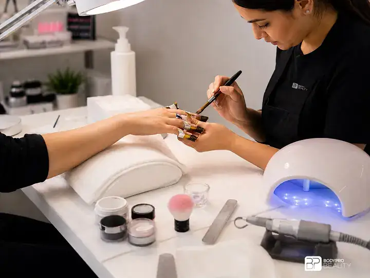 Student practicing gel and acrylic nail enhancement techniques with professional nail tools.